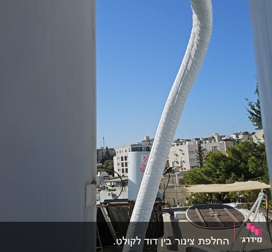 צינור מחובר לדוד שמש על גג עם רקע של בניינים ועצים